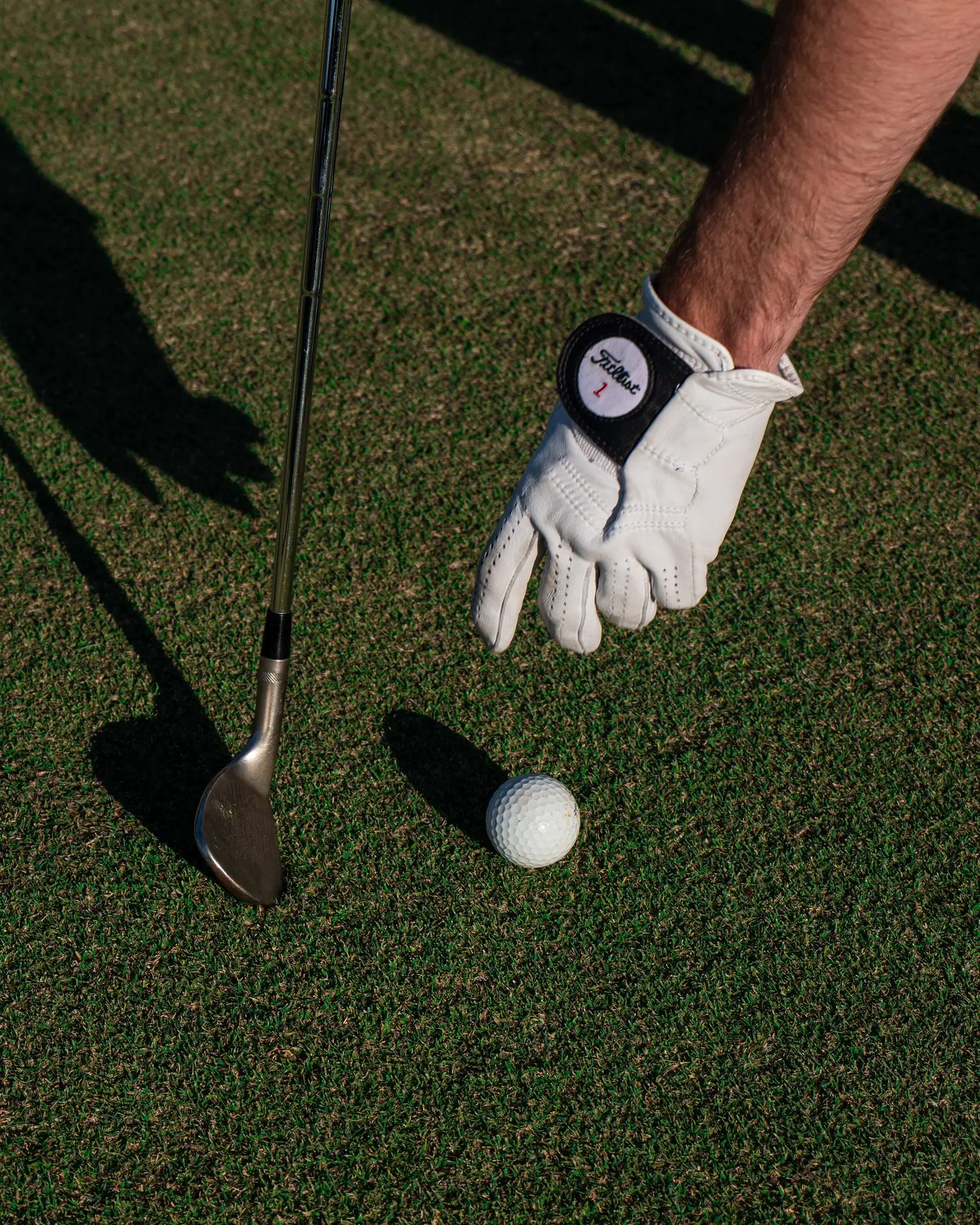 A gloved hand sets a golf ball beside a wedge